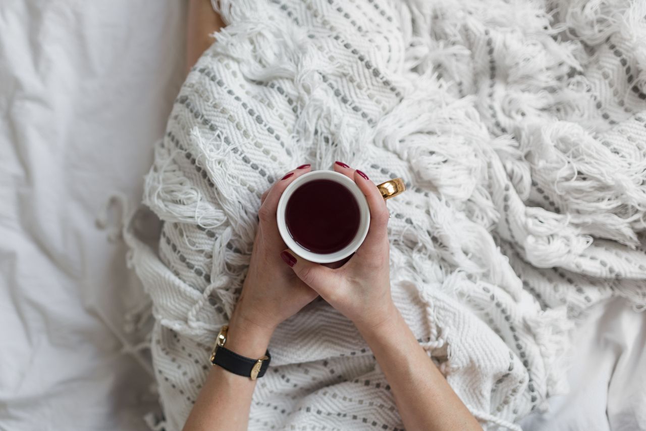 Soft photo of woman on the bed with the book and cup of coffee in hands